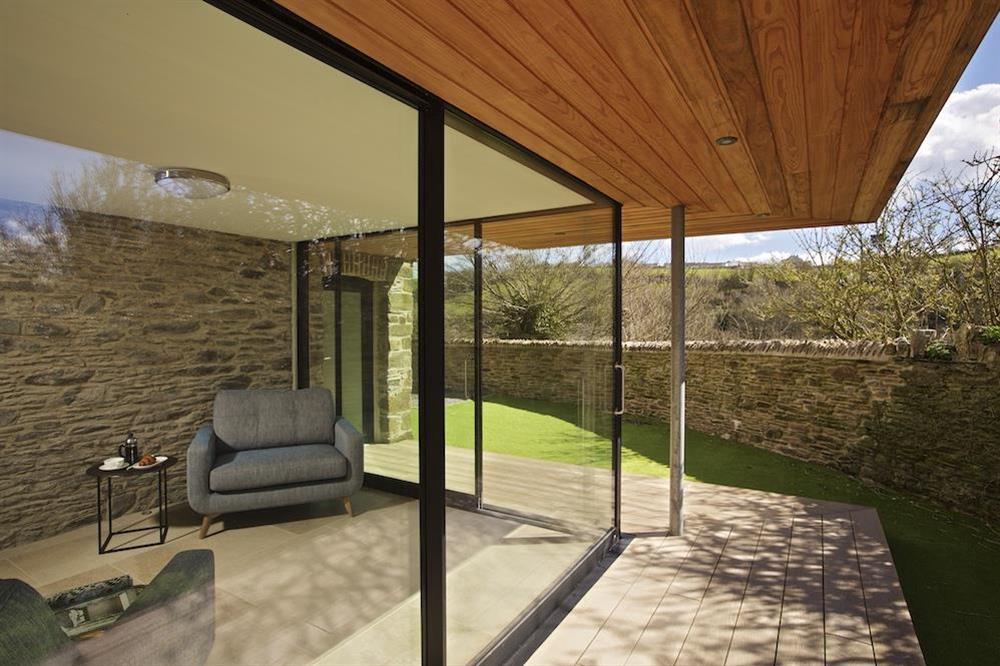 The sunroom adjacent to the kitchen with feature stone walls, sliding glass doors to the garden and two large love seats at The Old Milking Shed in , Bantham