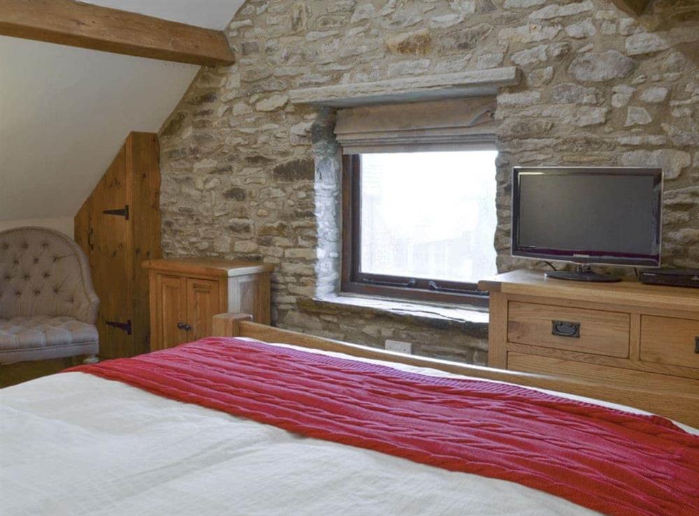 Double bedroom with exposed wooden beams and feature stone wall at The Old Stable in Barber Booth, near Whaley Bridge, Derbyshire