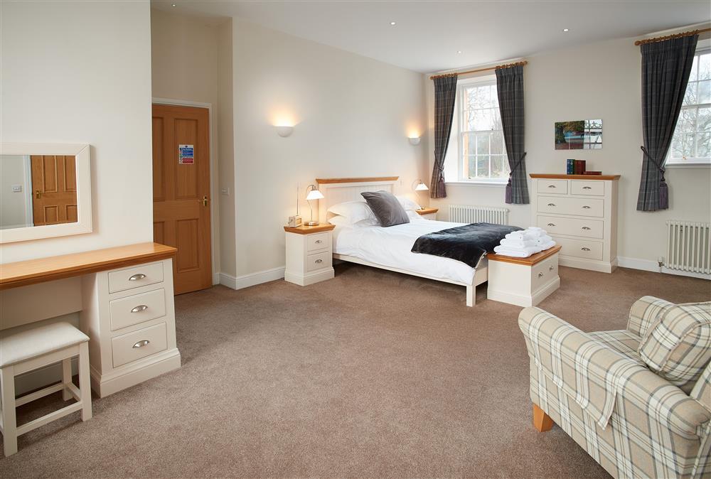Spacious bedroom with a 5’ king-size bed with dressing table and sofa at The Sir Walter Scott Apartment, Netherby Hall, Longtown