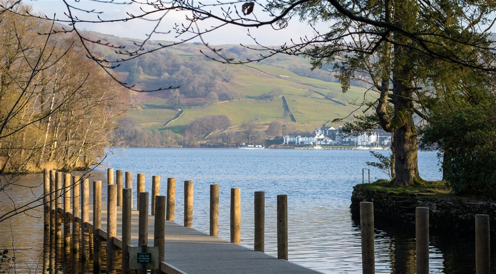 A jetty leading into a lake framed by autumn trees with mountains beyond at The Summer House in Nr Hawkshead, Cumbria