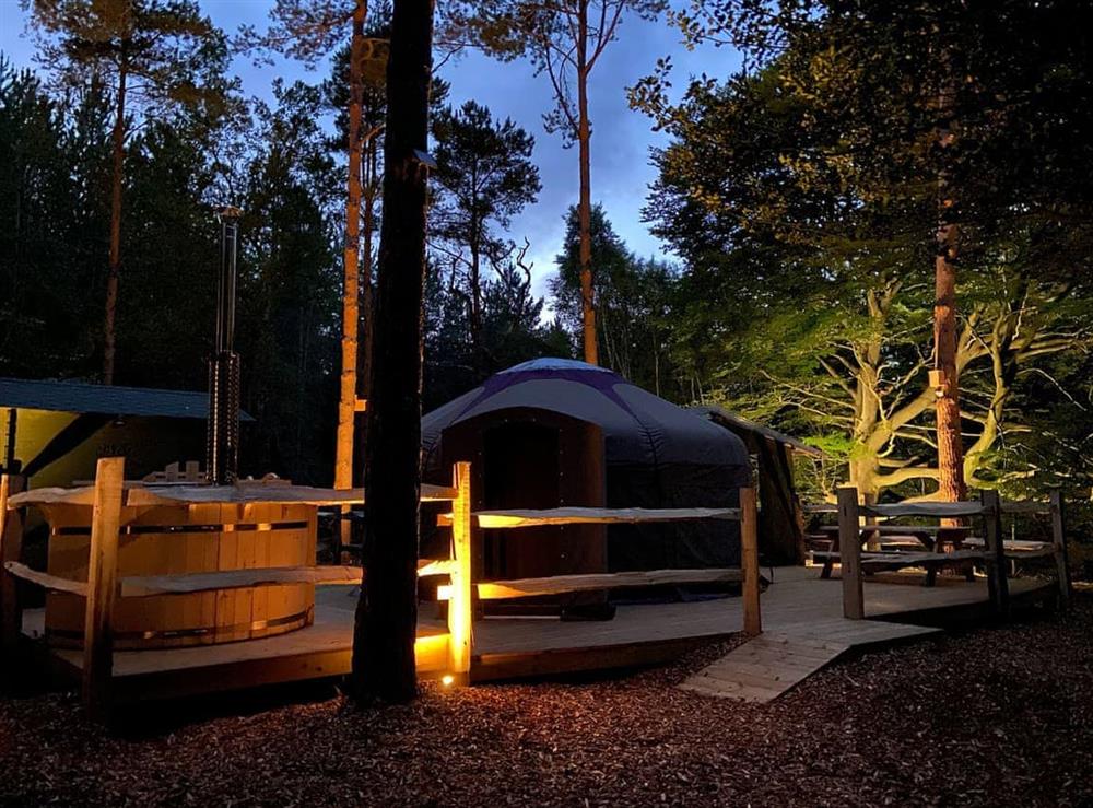Exterior and hot tub lit up at night at The Warren Yurt in Black Hill, near Crowborough, East Sussex