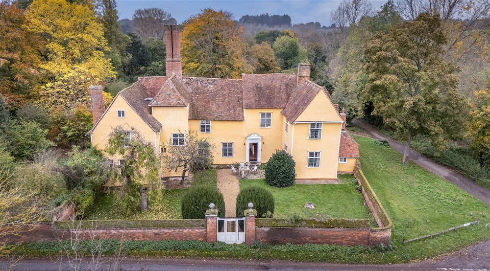 An aerial view of Thorington Hall and its walled southern garden, with patio, outdoor dining furniture, lawn and trees, Suffolk at Thorington Hall in Stoke By Nayland, Suffolk