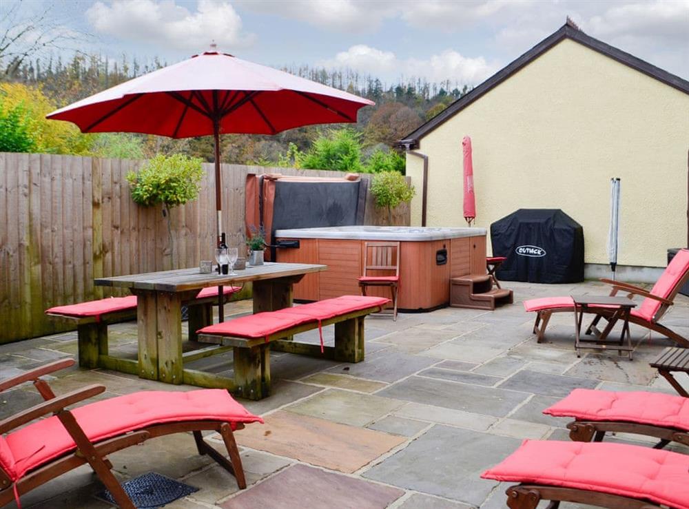 Large paved patio with table, loungers and a hot tub at Ty Glyndwr in Lower Cwm-twrch, near Llandovery, Powys