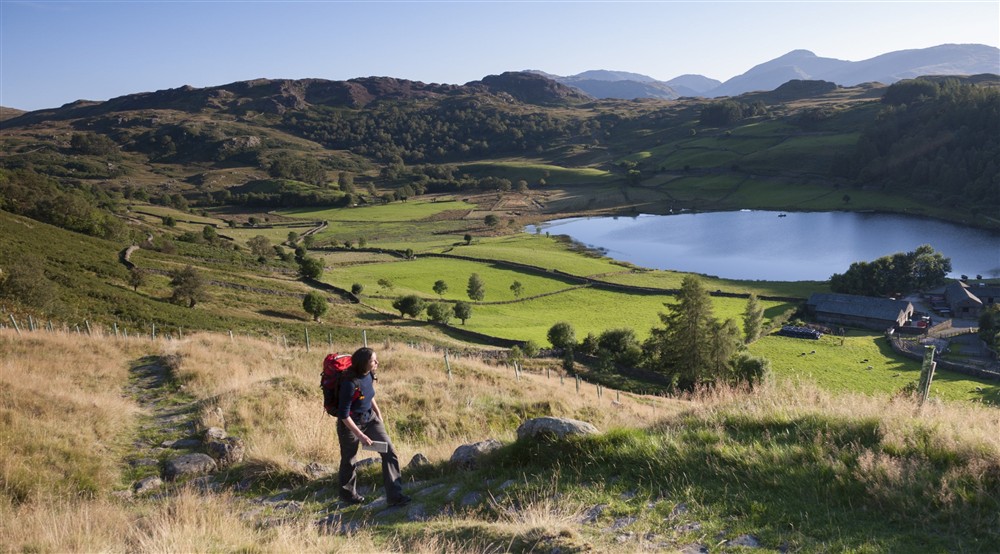 A walker enjoys the views of the village of Watendlath on a beautiful summers day at Watendlath Bothy in Keswick, Cumbria