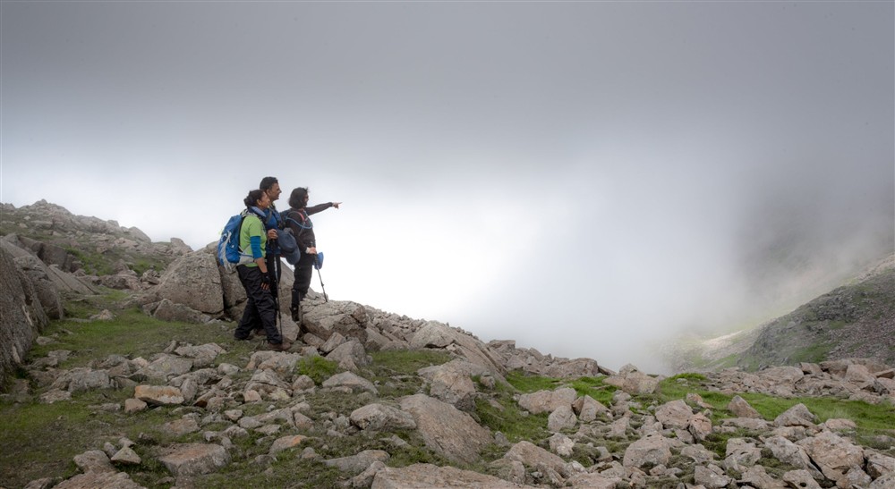 Hikers point out towards Great End from near the summit of Scafell pike on a misty summers day at Watendlath Bothy in Keswick, Cumbria
