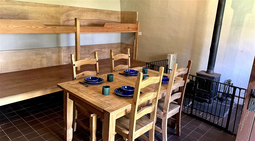 The sleeping platforms, dining table and woodburner in the living space at Watendlath Bothy in Keswick, Cumbria