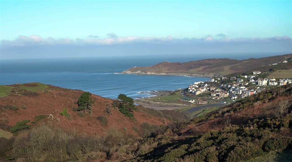 A scenic view of a small town by the ocean, captured from a hilltop, showcasing the coastline and surrounding landscape at West Challacombe Manor in West Exmoor, Devon
