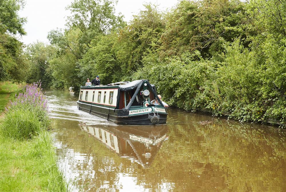 Narrowboat gracefully cruising along the South Stratford Canal at Wharf Cottage, Wootton Wawen